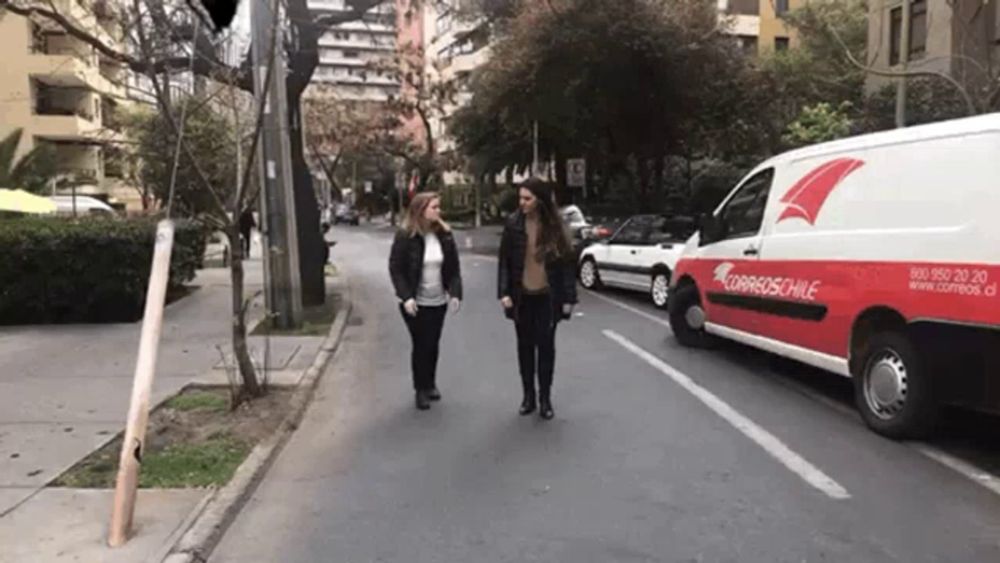 two women are walking down a street next to a van that says correos chile