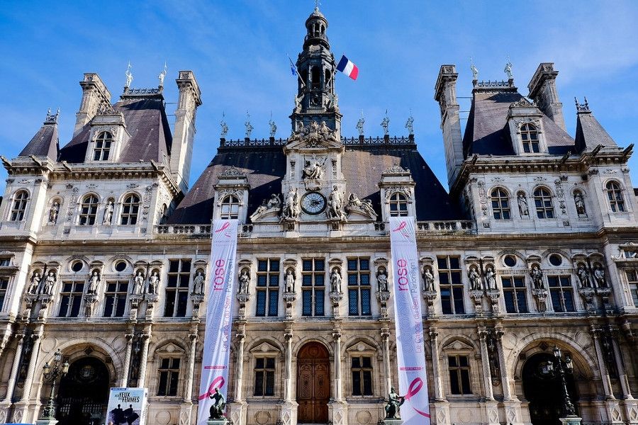 Face de la mairie de Paris avec banderoles octobre rose. Le ciel est bleu.