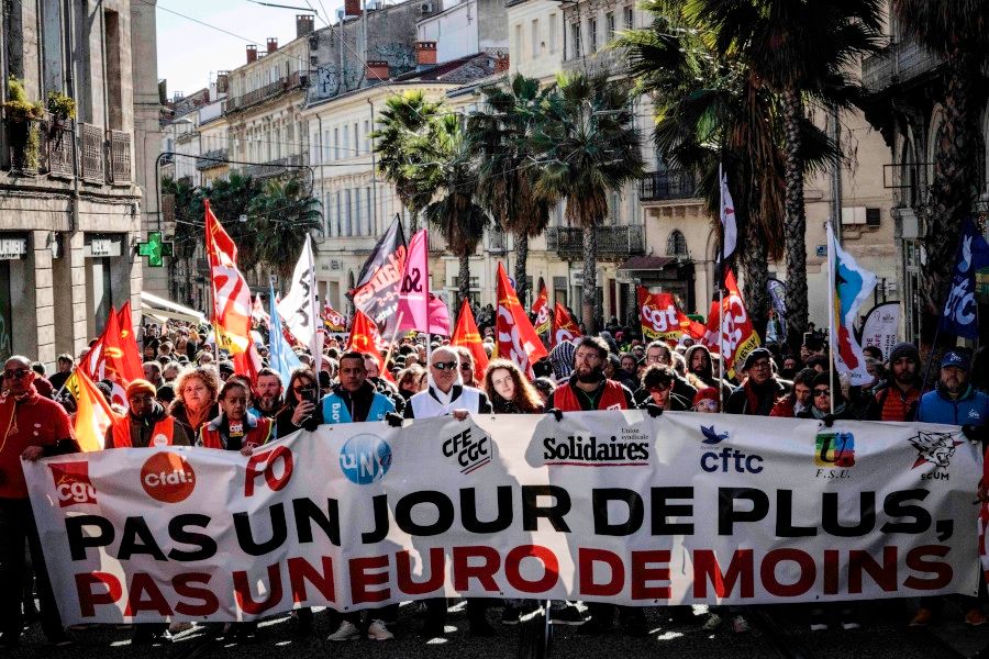 Banderole intersyndicale "pas un jour de plus, pas un euro de moins". De nombreux syndicalistes aux gilets de multiples couleurs la portent. On aperçoit des palmiers derrière.