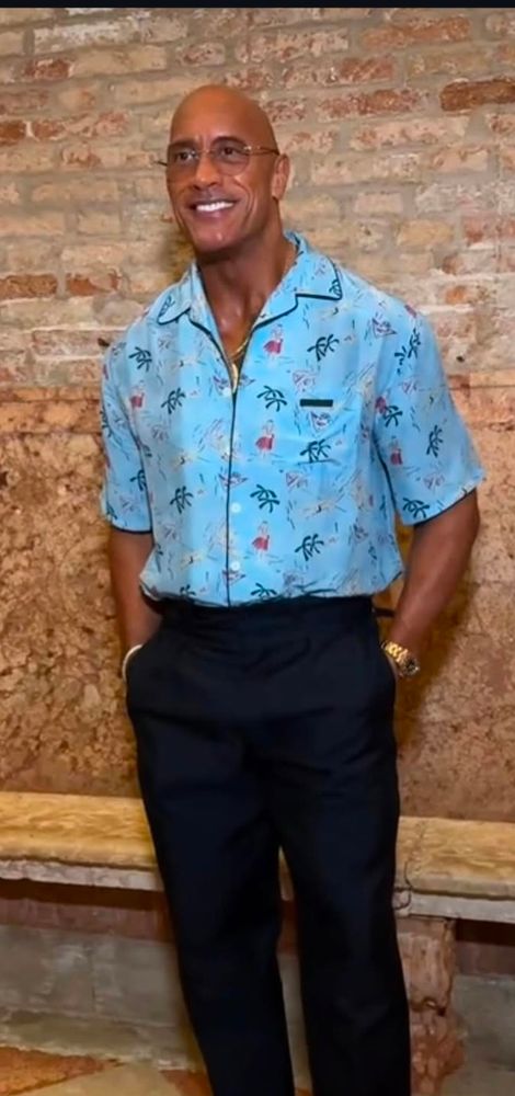 The Rock in blauem Hemd vor einer Ziegelwand