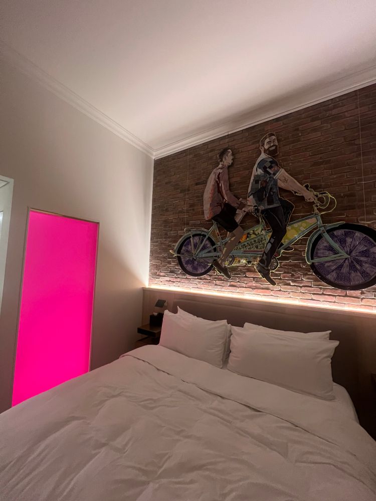 Hotel room with a comfy bed, a pink glass bathroom window and two men staring at me from the bicycle 