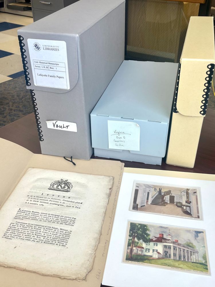 Three archival boxes from SCUA collections in the background on a desk. A letter from the Lafayette Family Papers and two postcards from Mount Vernon are in the foreground. 