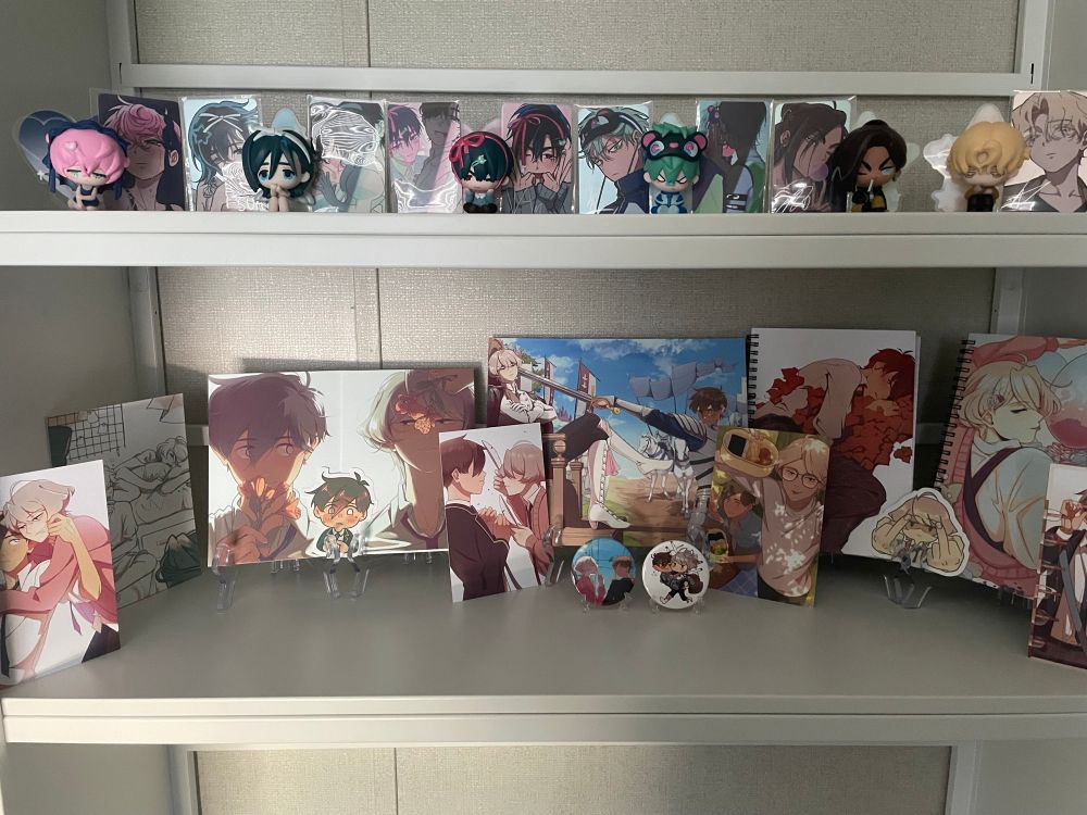 A white book shelf with merchandise from the YouTube series Alien Stage and the webtoons comic Our Walk Home displayed.