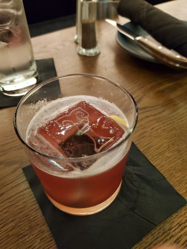 A whiskey sour with a giant ice cube with the letter T