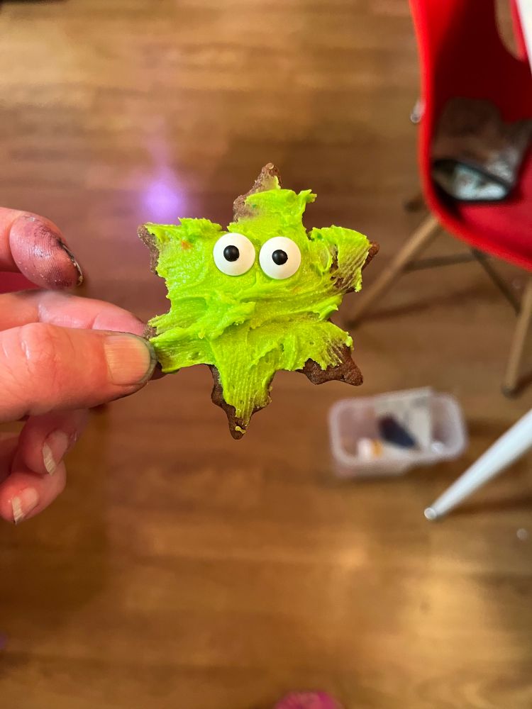 A snowflake cookie frosted with electric green frosting. It has comically large candy eyes that make it look like it's staring right through your soul.