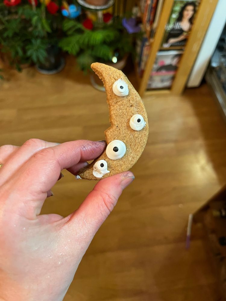 A crescent moon-shaped cookie, bare except for four candy eyes scattered haphazrdly across it.