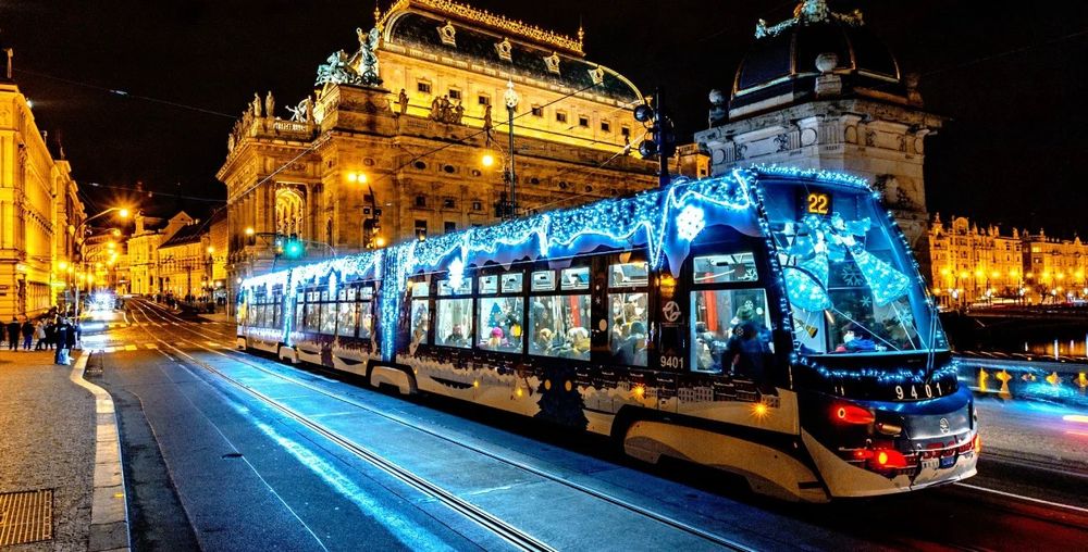 A tram in Prague, arriving at Národní divadlo tram stop. The tram is fitted with Christmas lights on the outside. 