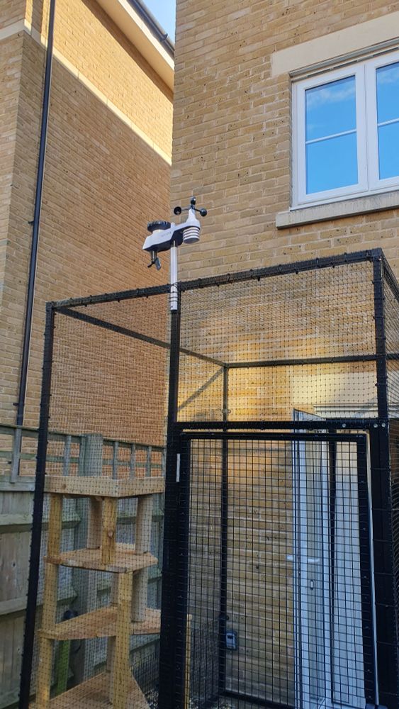 Auf dem Foto ist die Wand eines Hauses zu sehen, mit einem Katzengehege, auf dem eine kleine Wetterstation installiert ist.