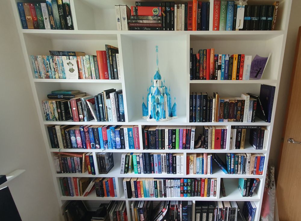 Photo of a large white bookshelf. A special shelf in the middle displays the Ice Castle from Frozen in Lego.