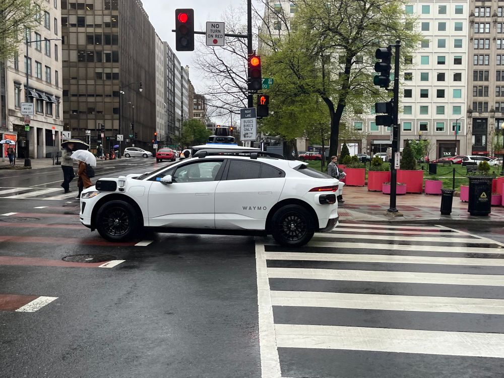 A white WayMo car driving past a crosswalk in Washington, D.C.