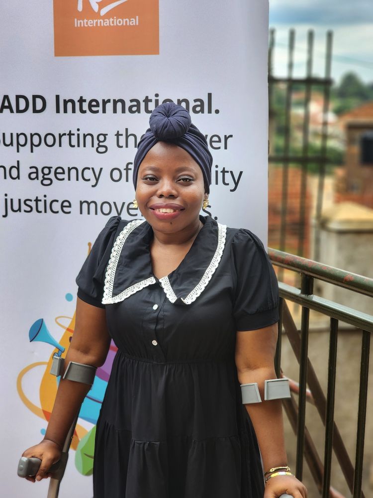 A picture of Shamim wearing a black dress and a navy-blue head wrap. She is holding clutches.