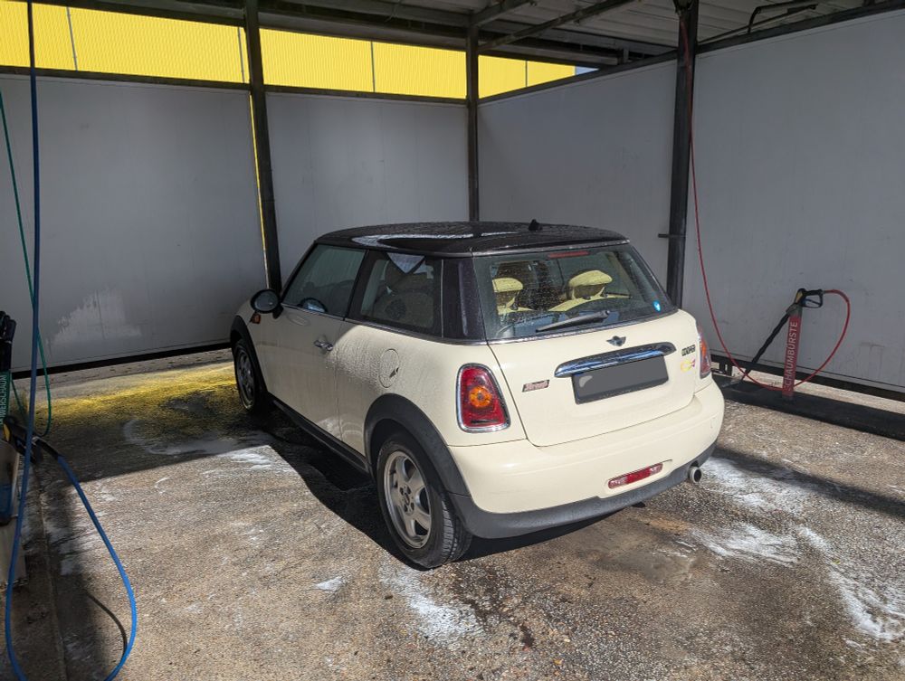 Photo of a dripping wet Mini Cooper in a self service car wash. It's glistening and the floor around it is covered in traces of foam.
