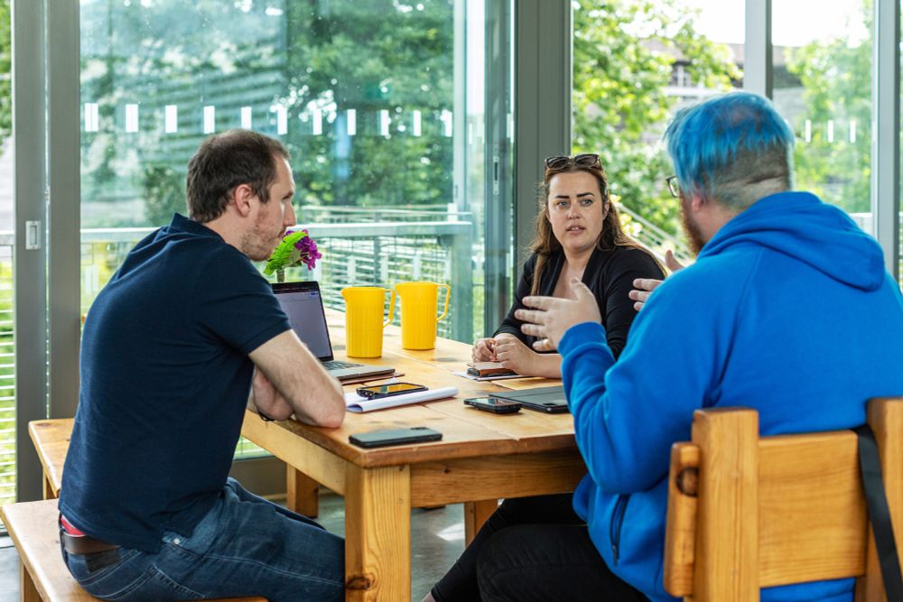 Three people sitting around a table discussing Agilebase software. Two men, one woman, light and airy setting