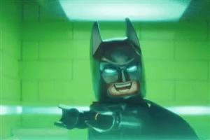 a lego batman is standing in front of a green brick wall