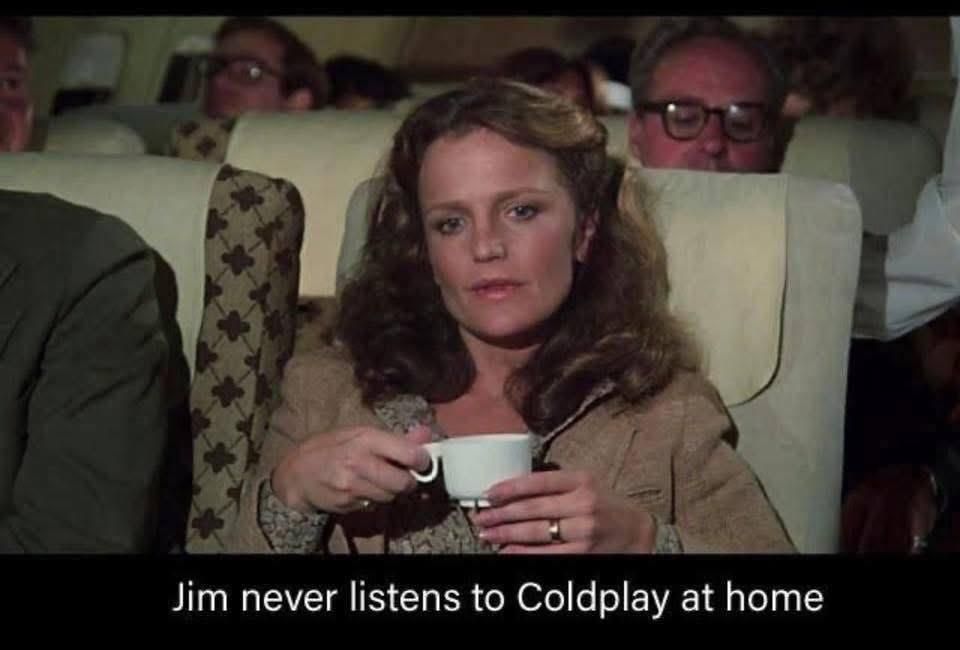 A still from a scene in the movie Airplane! It depicts a white woman in her 30s sitting in an airplane seat and holding a white cup of coffee. The caption reads "Jim never listens to Coldplay at home," which is similar to the dialogue in this actual scene in the actual movie.