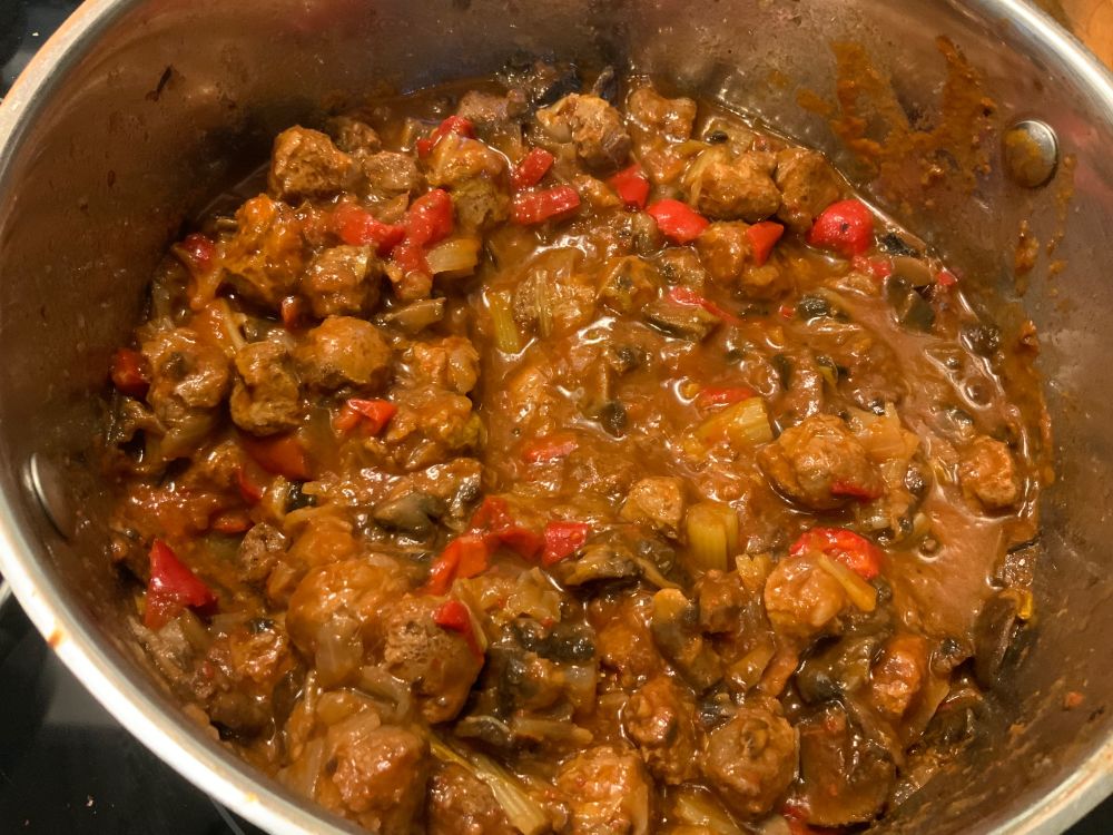 a large stainless stew pot full of a red, meaty looking stew with chunks of red bell pepper in it