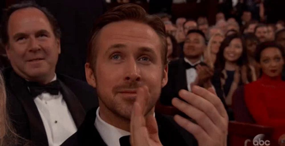 a man in a tuxedo is applauding while sitting in a crowd of people .