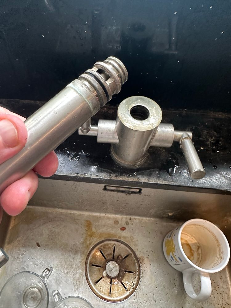 Hand holding spout removed from double tap on kitchen sink below. 