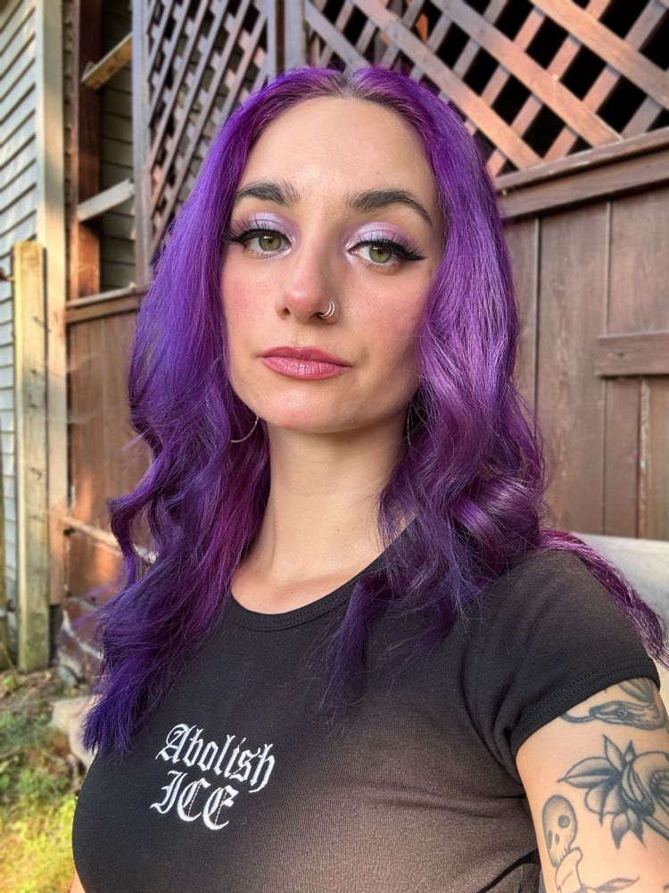 Jupie selfie sitting outside in the backyard. She is wearing a black shirt that has text Abolish ICE 