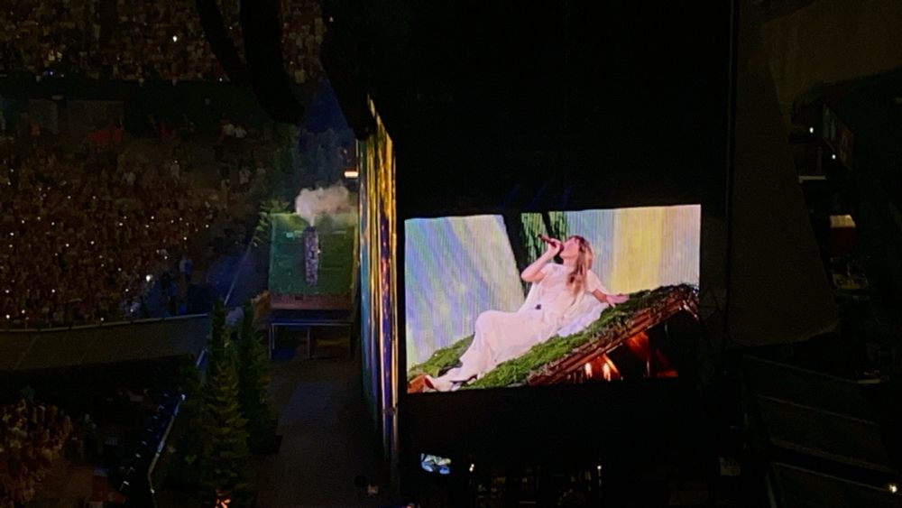 Folklore: Taylor in a flowing cream dress on the roof of a mossy cabin 