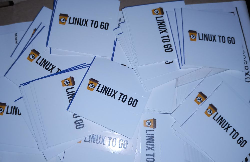 Ein Haufen Sticker. Auf jedem Sticker steht neben einem Kaffee to go-Becher mit Piratenlogo in schwarzer Schrift Linux to go.