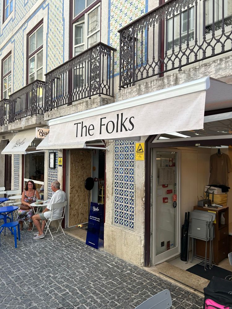 an awning over a coffee shop in lisbon. the awning is cream colored and in a navy blue font, the awning's text reads The Folks