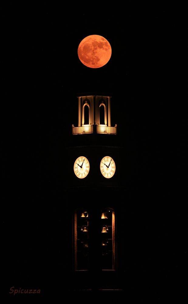 An orangey full moon over a clock tower.