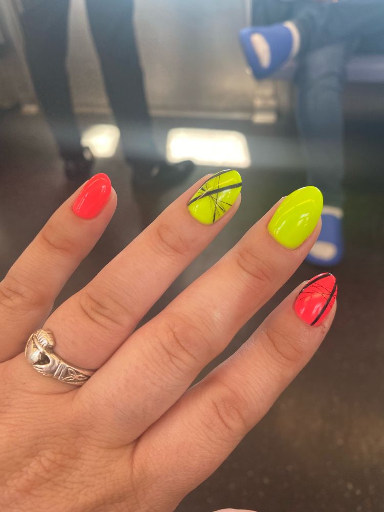 Left hand with claddagh ring. Pinkie nail and index nails are hot/neon pink. Ring and middle nails are hot/neon green. The ring and index have a black graphic nail design 