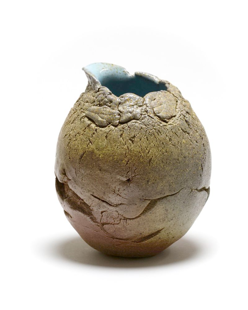 Grape-fruit sized pouring vessel, with textured surface cause by hand-pinching the speckled stoneware clay. Toasty brown near the base with yellows and grey near the shoulder, yellow ash droplets on grey, and a pale robin's egg blue glaze inside.