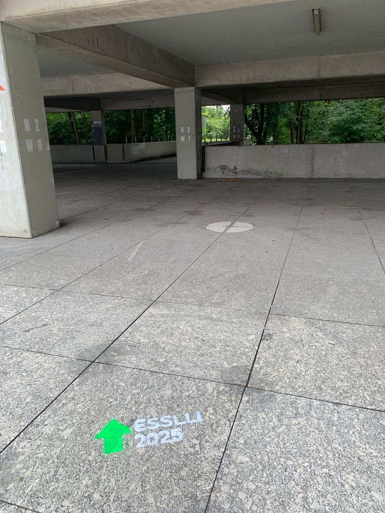 Concrete path with  “ESSLLI 2025” and a large arrow sprayed in green and white chalk
