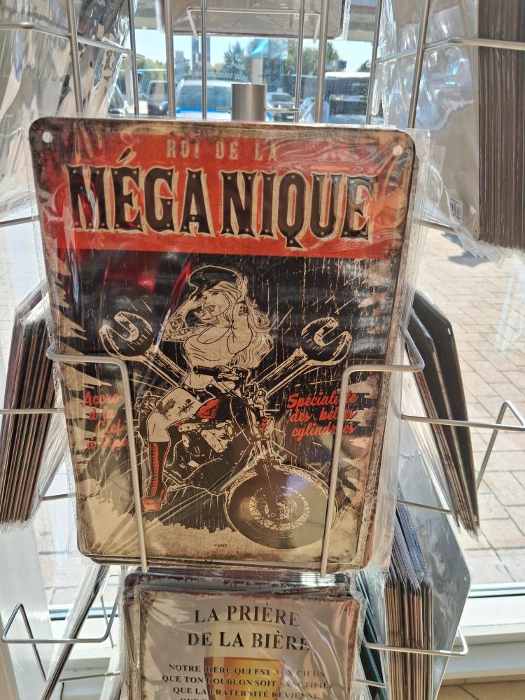Une plaque en métal avec écrit "Roi de la méga nique" (ça fait un jeu de mot avec mécanique, krr krrr), dessous y a une demoiselle sur une grosse moto 