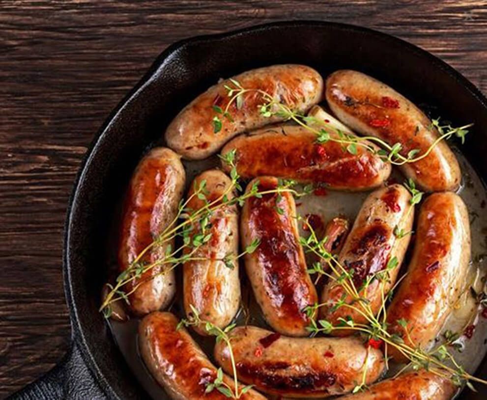 a bunch of sausages in cast iron skillet with a few sprigs of thyme