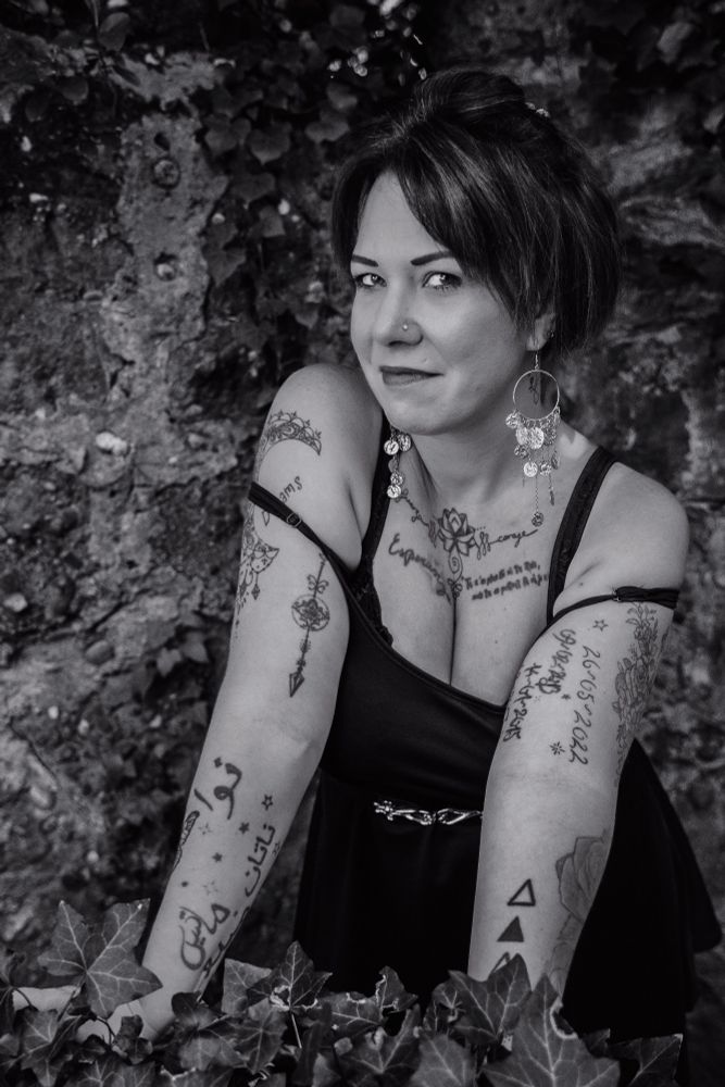 Photo noir & blanc cadrage plan taille d'une femme légèrement penchée en avant, les bretelles de sa robe glissées sur ses bras.