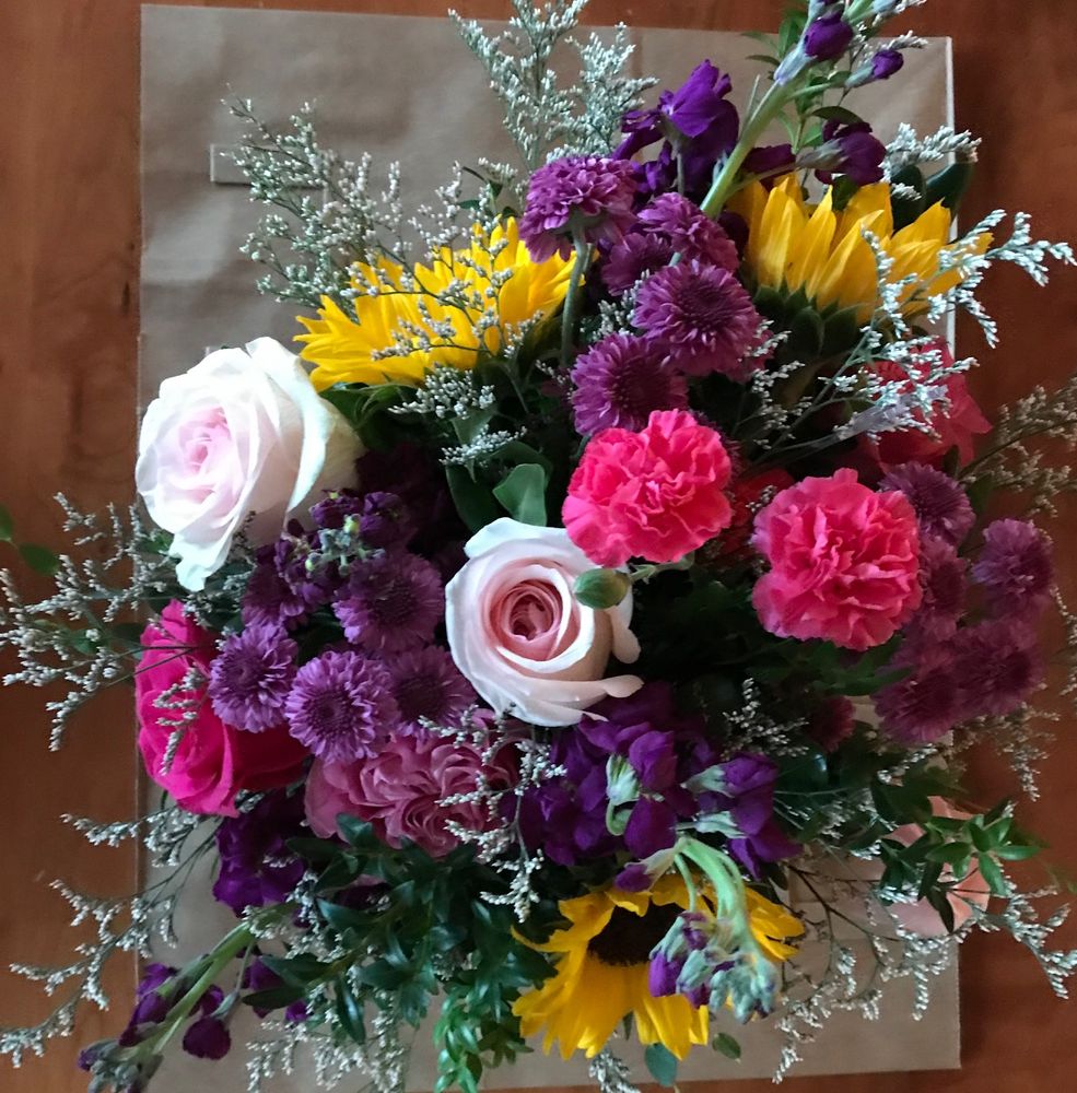 A bouquet from above, with pale pink roses, bright pink carnations, sunflowers, purple mums, and baby's breath.