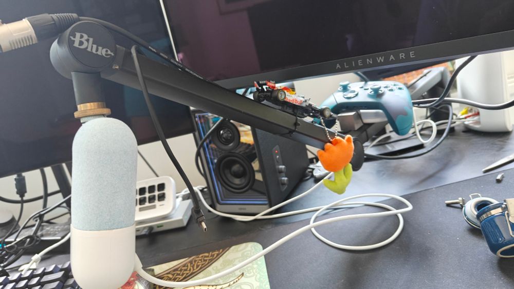 A mic arm with a tiny microphone on the end and various items to weigh it down (F1 car model, tungsten cube, mic base, Xbox controller).