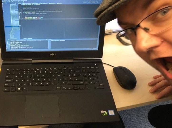 A laptop computer sits on a desk. On the screen is code for the software Janeway. To the right a man, Martin Eve, looks very excited. 