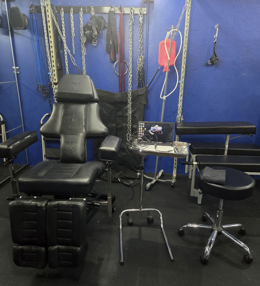 Office chair with a stool, desk with a computer, tube camera and an enema device in the background.