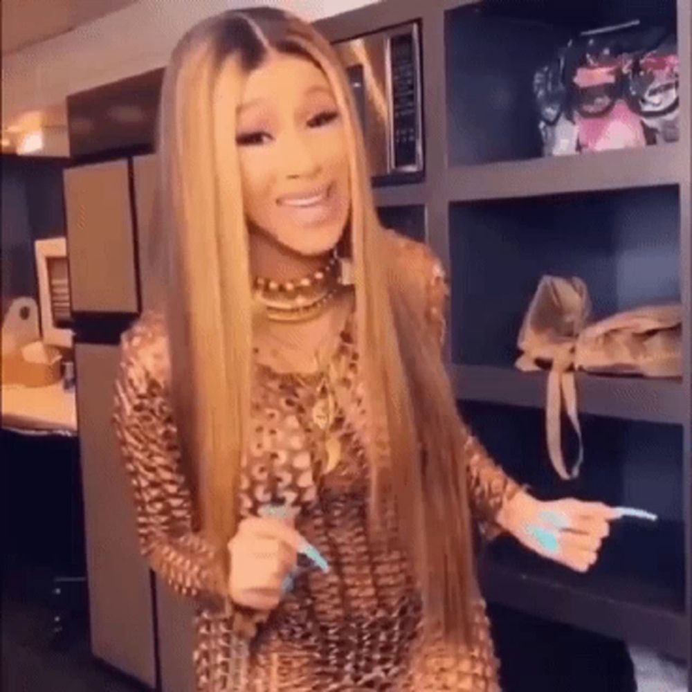 a woman with long blonde hair is standing in front of a microwave in a kitchen holding a toothbrush .