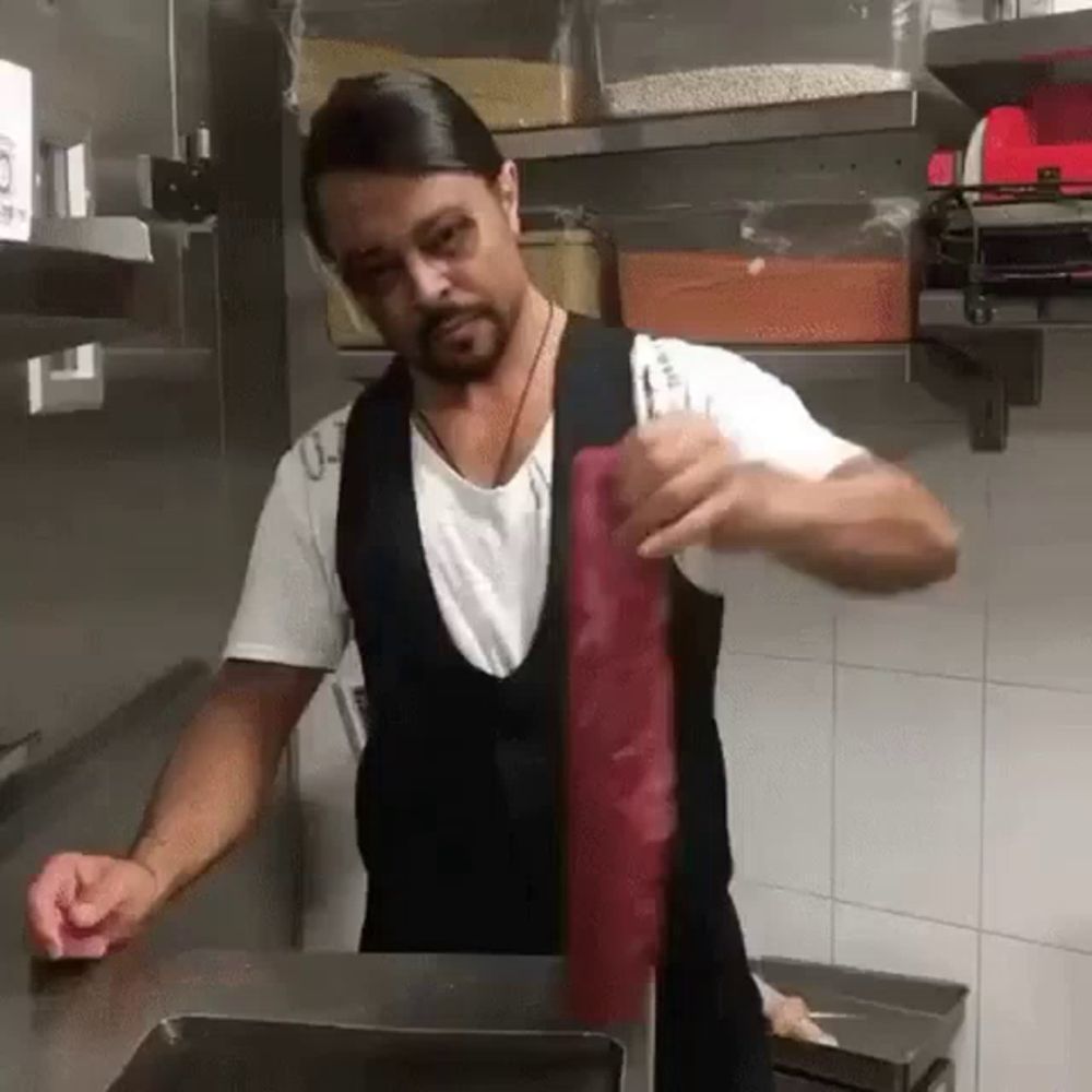 a man is standing in a kitchen holding a piece of meat in his hand .