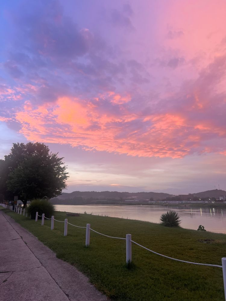 Sundown with pink blue skies tree on the left on a riverbank, small fencw post thru the front Appalachia