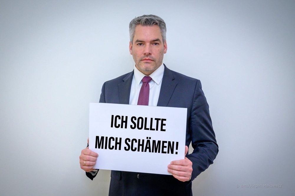 Karl Nehammer hält ein Plakat mit den Worten "ich sollte mich schämen!"
