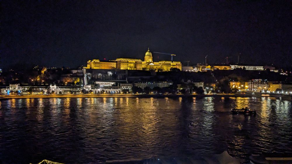 Lighting the Danube - View from the Hotel Intercontinental Budapest September 2024 - The Buda Castle is light giving a yellow glow, while lights along the river front reflect gracefully on the river with orange and white, a small ferry leaves a gentle wake behind it as it travels along the river.