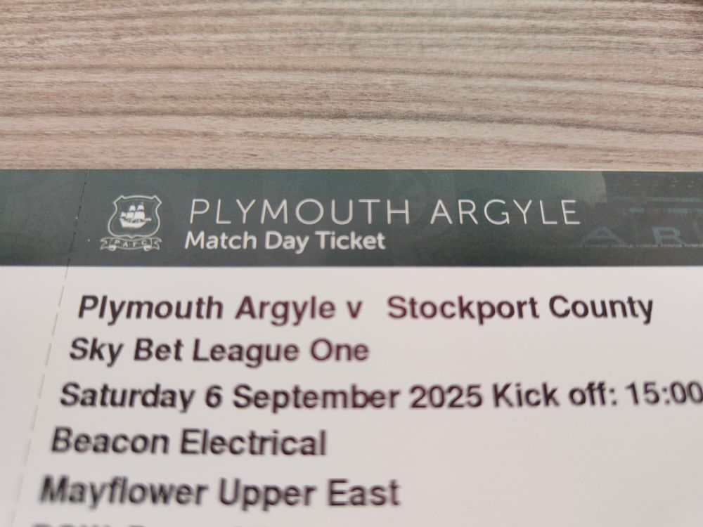 A football ticket on a table. The top is green with the Plymouth Argyle logo and the words Plymouth Argyle Match Day Ticket. The rest of the ticket is text about the match 