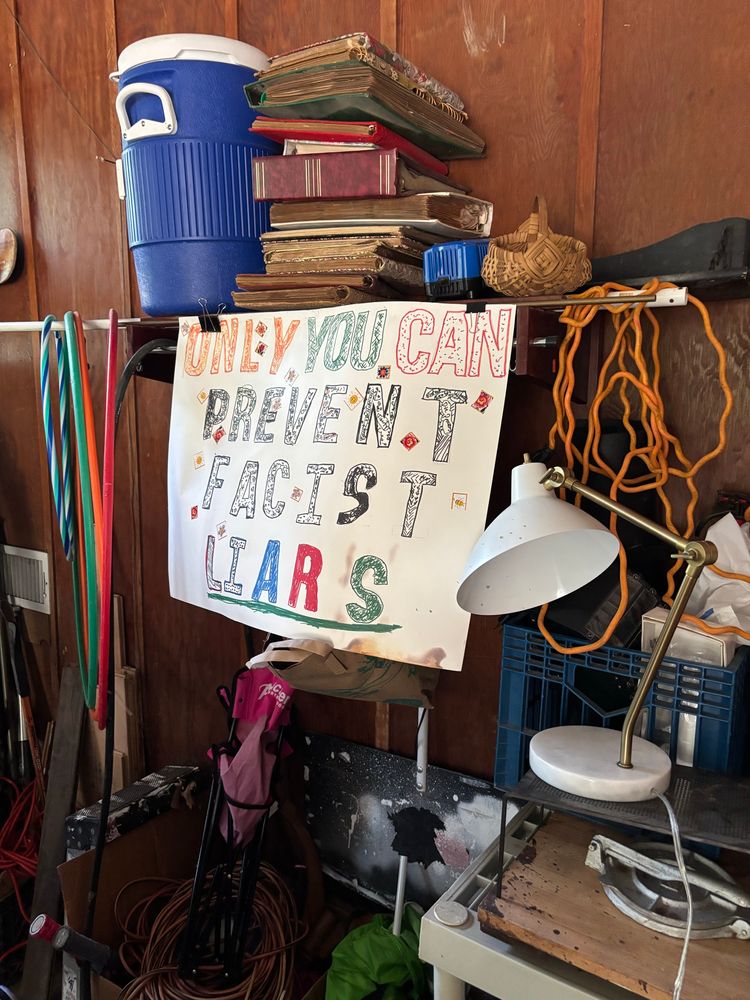 Photo of a cluttered garage with protest sign visible: ONLY YOU CAN PREVENT FASCIST LIARS