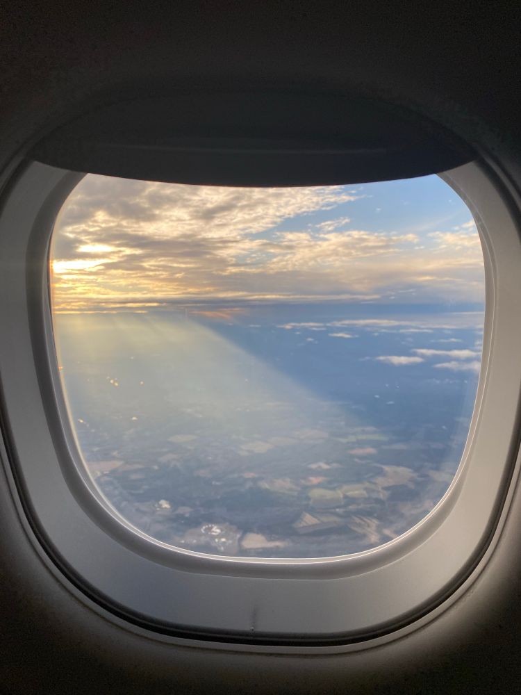 A view out the airplane window with shafts of light shining on rivers. 