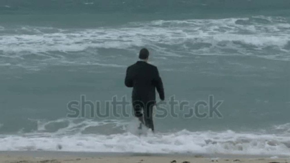 a man in a suit is walking into the ocean .