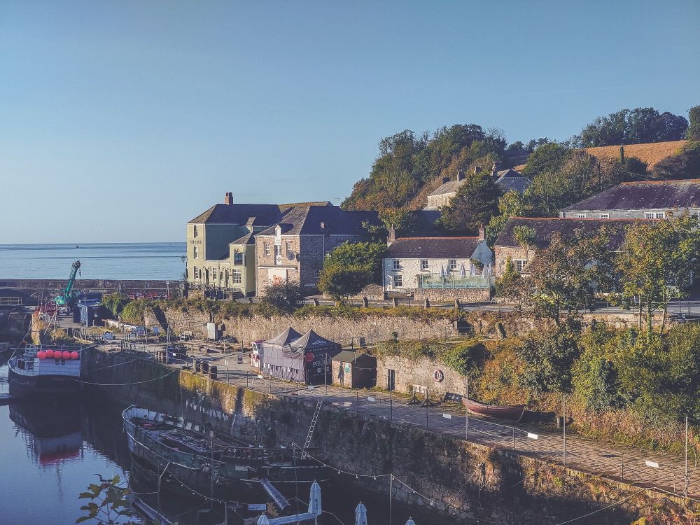 A picture of the harbour at Charlestown in Cornwall early in the morning with blue skies and bright sun light hitting the buildings 