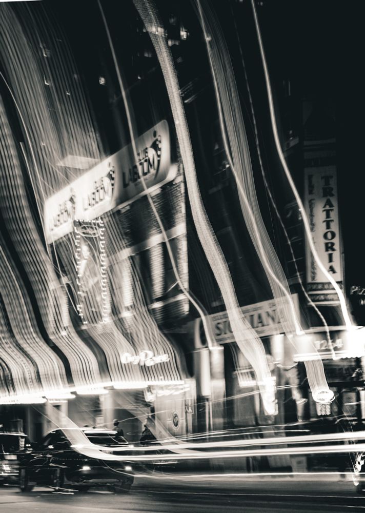 Black and white long-exposure photo of Place des Arts in Montreal. Vertical light trails ripple across the frame, creating a dreamy, abstract city night scene with blurred motion and glowing streaks.