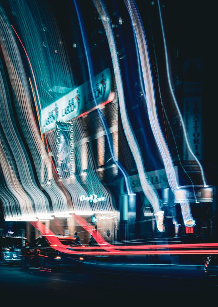 Color long-exposure shot of Place des Arts in Montreal. Neon blue and red light trails cut through the dark night, capturing the vibrant energy and movement of the city streets