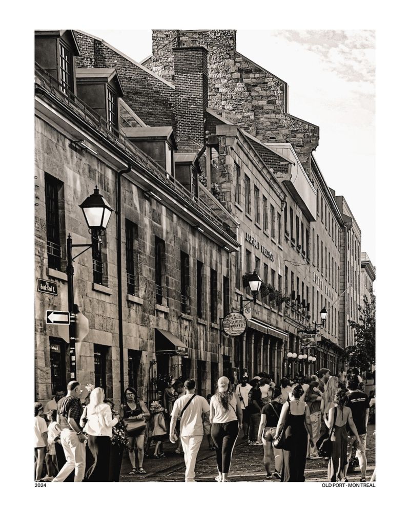 Black and white photo of a peaceful cobblestone street in Old Montréal. A person is seen riding a bicycle into the distance, framed by historic stone buildings on either side. The mood is calm and nostalgic, with soft light and vintage tones evoking a timeless charm.